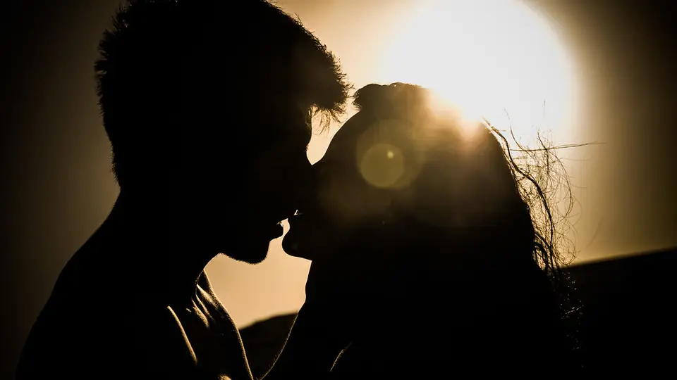 Silhuet af et par, der kysser i modlys fra en lav sol, et billede på kemien ved sexdating