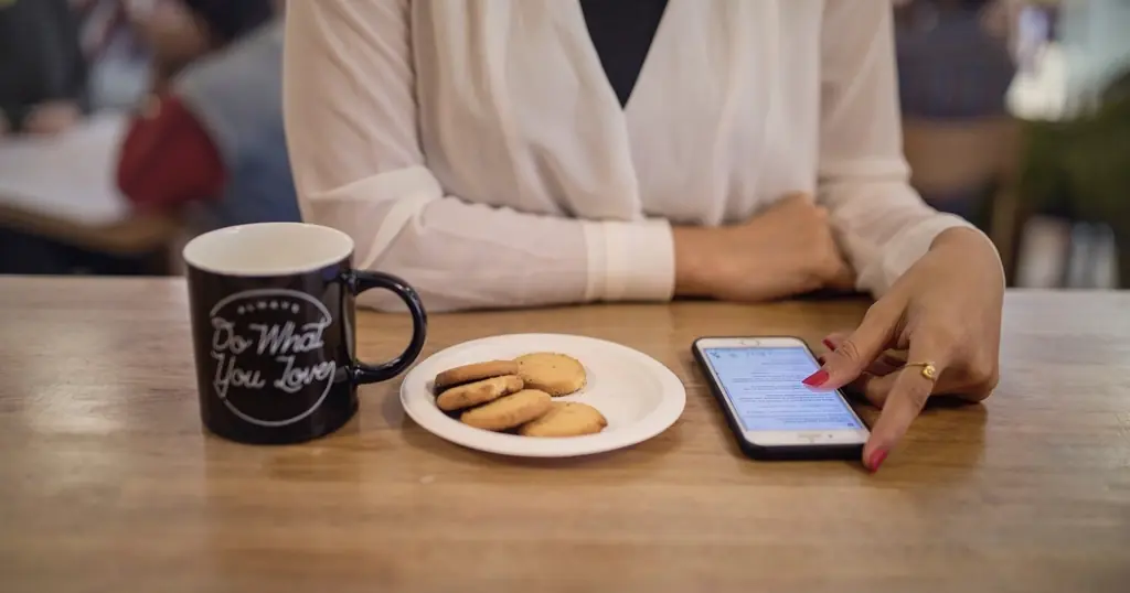 Sikker sexdating: en kvinde holder sin telefon ved et bord med en kop kaffe